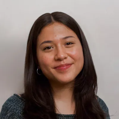 A young woman with long dark hair and a gentle smile is pictured against a plain background. She is wearing a dark sweater and hoop earrings.