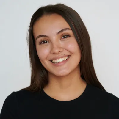 A young woman with straight dark hair and a warm, broad smile showing her teeth, wearing a simple black short-sleeved crewneck t-shirt against a plain white background.