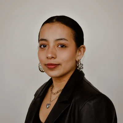 Young woman with hair pulled back in a bun, wearing a black leather jacket, hoop earrings, and layered necklaces. 