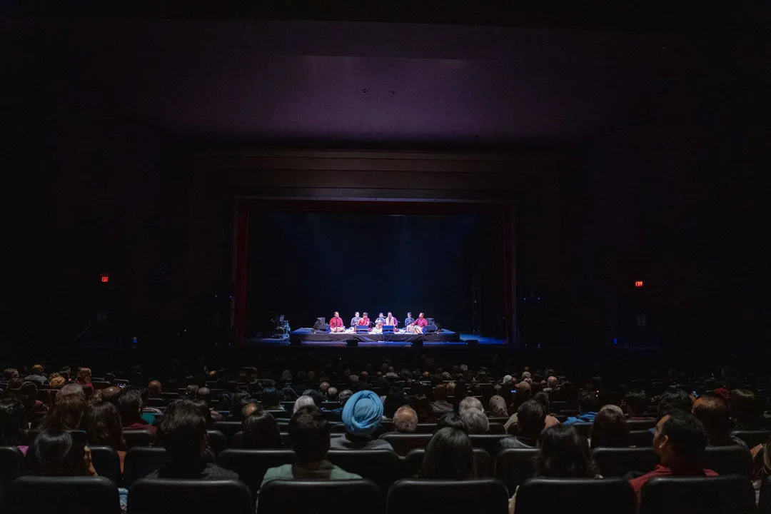 A full house watching a seated qawwali ensemble lit in blue on the Chrysalis proscenium stage