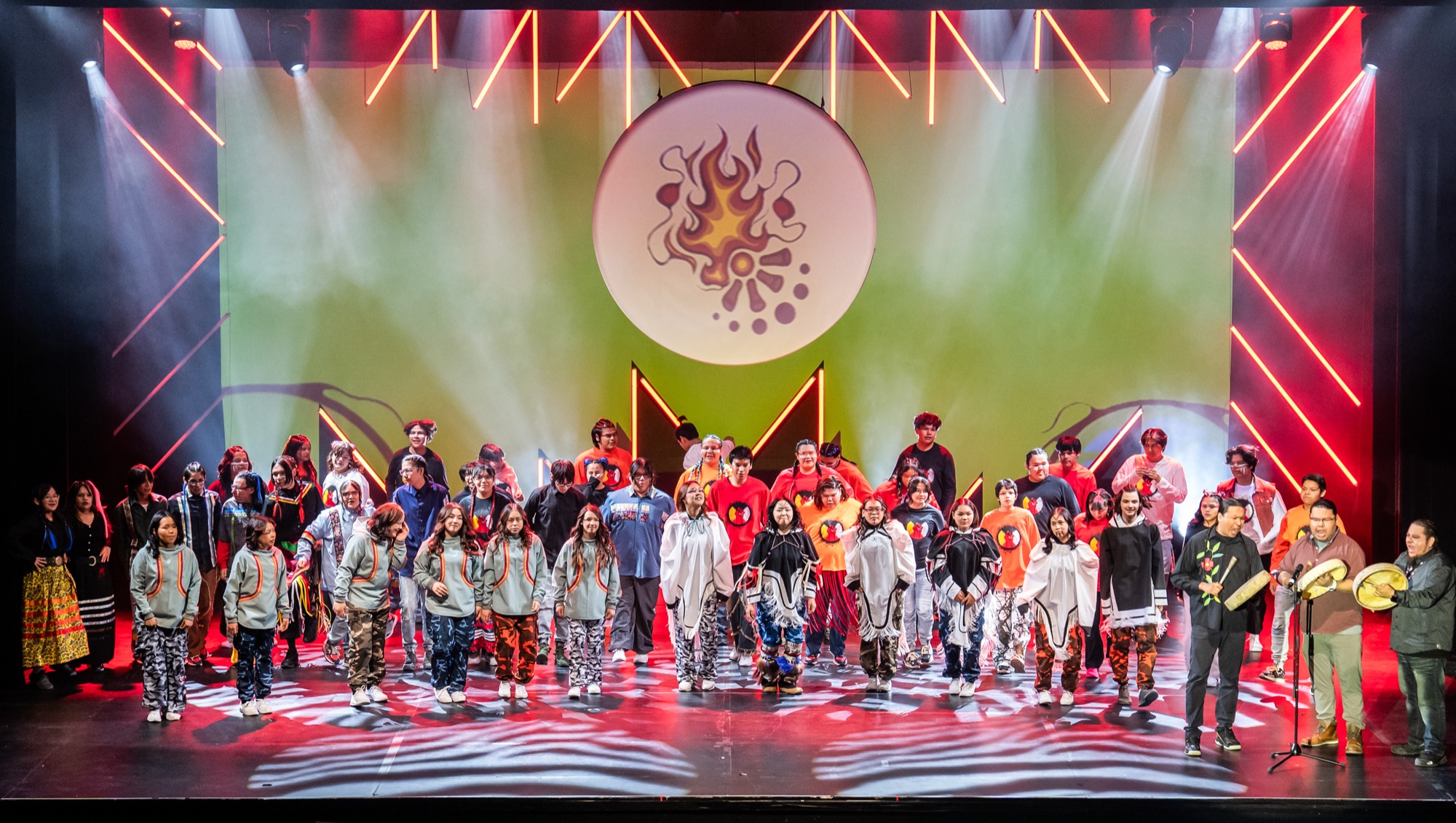 A large cast filling the Chrysalis stage under coloured light at the end of a performance